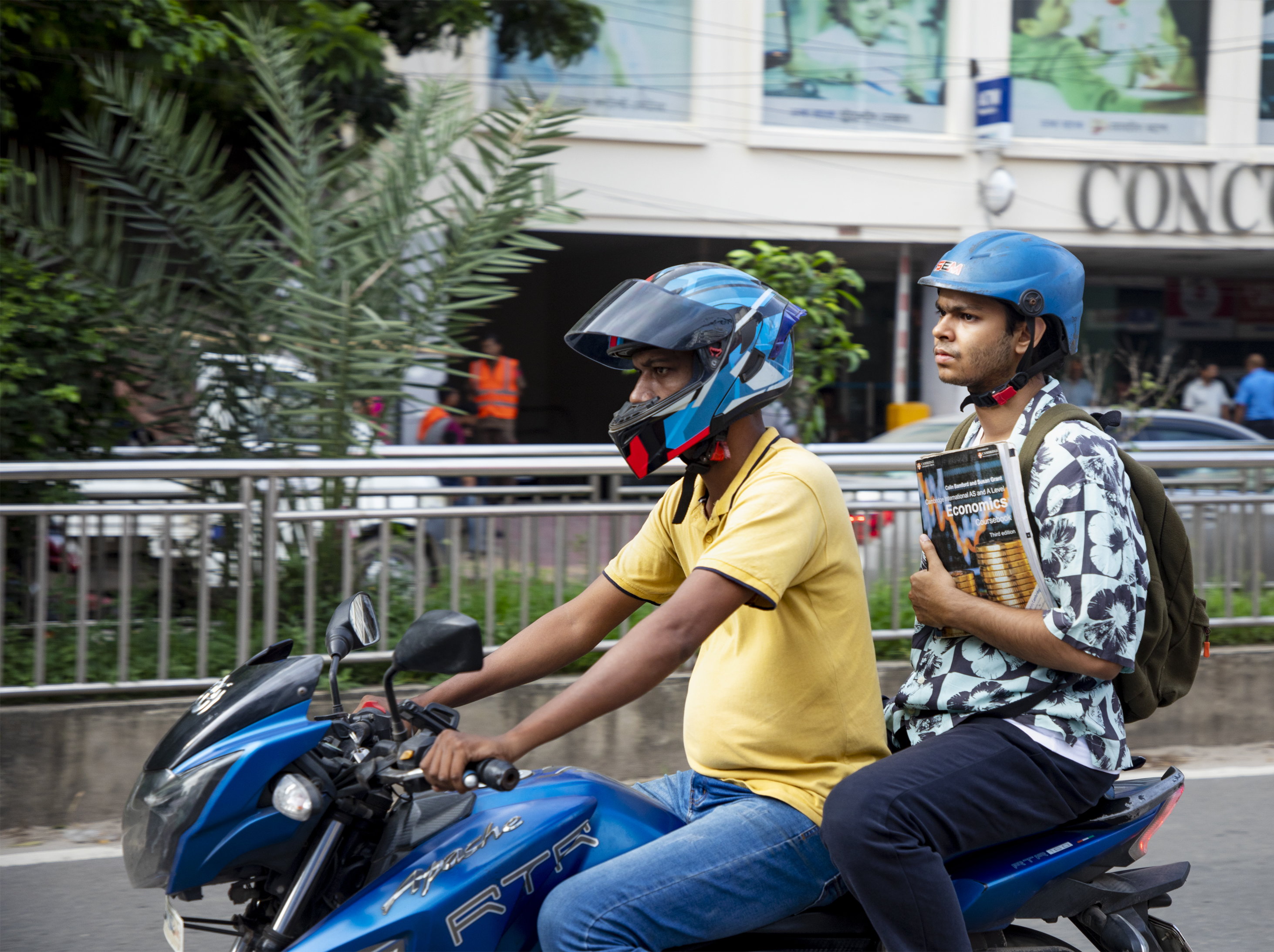 Student, sat behind a bike rider, on a motorcycle.