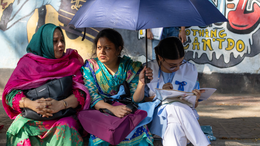 A parent holding an umbrella over their child who is studying