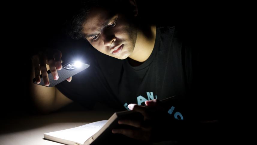 A photo of a boy studying with his phone's flashlight