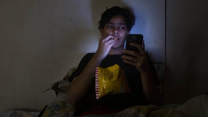 A person eating chips and using their phone