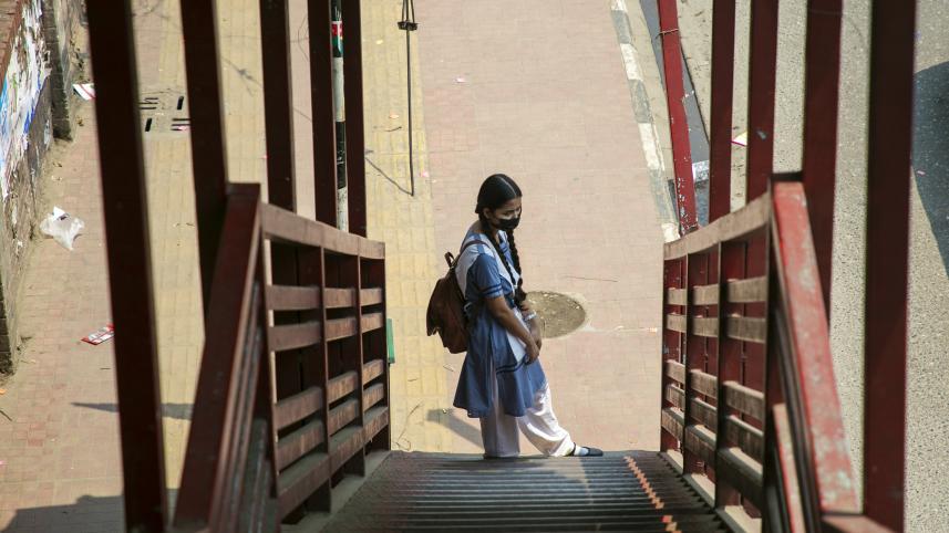 A student seen standing on the footpath, likely waiting for a bus.
