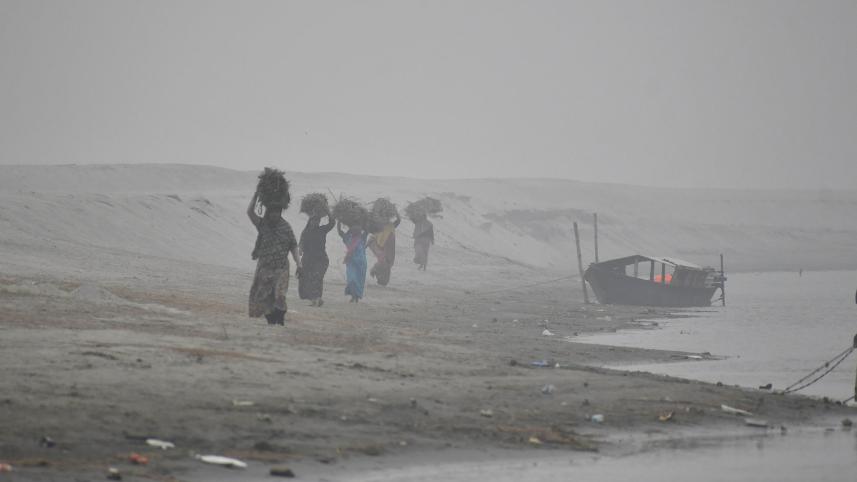 Women on their way home amid dense fog after collecting firewood, mostly branches of trees, from a char in the Brahmaputra. People from low-income families are struggling to make ends meet as their income has shrunken due to bad weather.