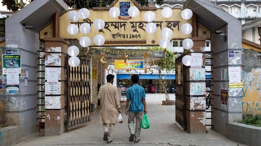 Two students walking in through the main entrance of their dormitory hall with each one carrying a bag consisting of iftar.