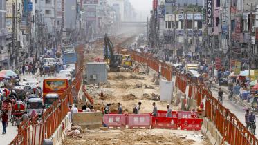 People crossing the street through the construction site of the metro railway.