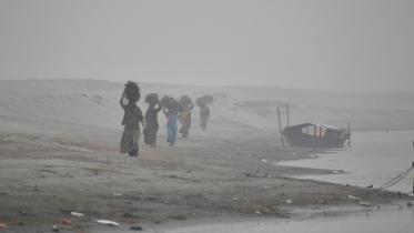 Women on their way home amid dense fog after collecting firewood, mostly branches of trees, from a char in the Brahmaputra. People from low-income families are struggling to make ends meet as their income has shrunken due to bad weather.