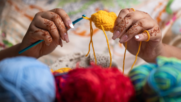 Artist crocheting with a yellow thread while three other shades of yarn are laid out in front of them. 