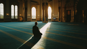 Person praying in a mosque with a sliver of sunlight pouring in.