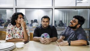 A man with a poker face sitting with two laughing friends.